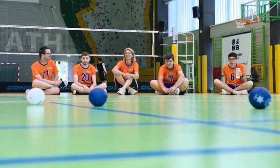 Zawodnicy z niepełnosprawnościami siedzą na parkiecie hali sportowej UBB